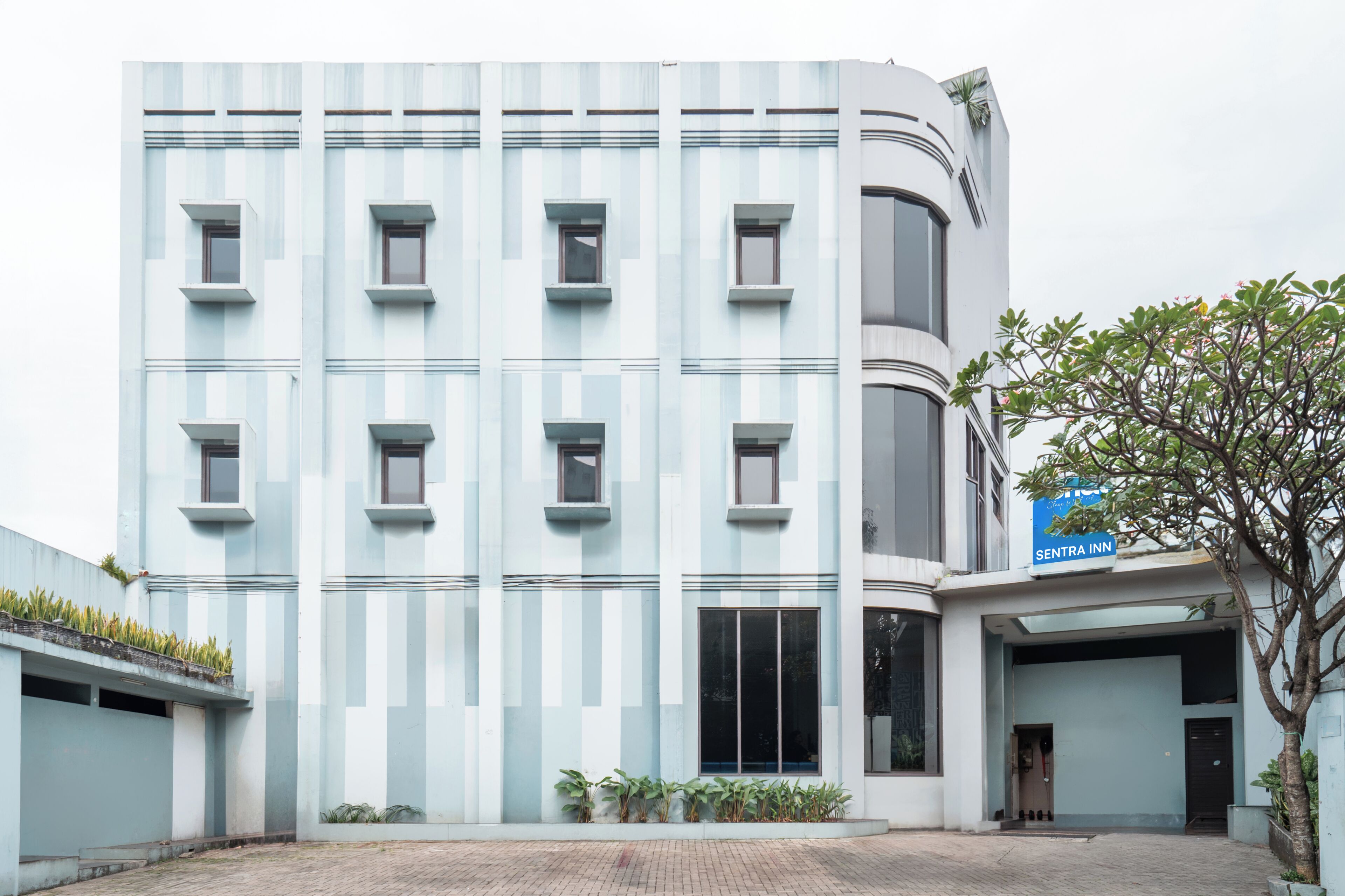 A modern building with a light blue facade, multiple windows, and a sign for 'SENTRA INN' on the right.