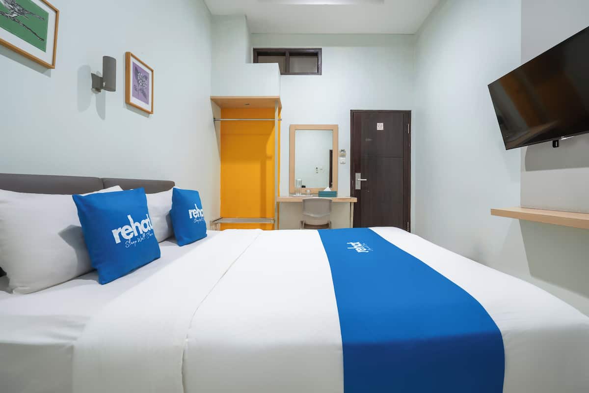 Une chambre d’hôtel équipée d’un lit, d’un bureau, d’une chaise, d’une armoire, d’un miroir et d’un téléviseur fixé au mur.