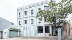 A modern building with a light blue facade, multiple windows, and a tree in the foreground.