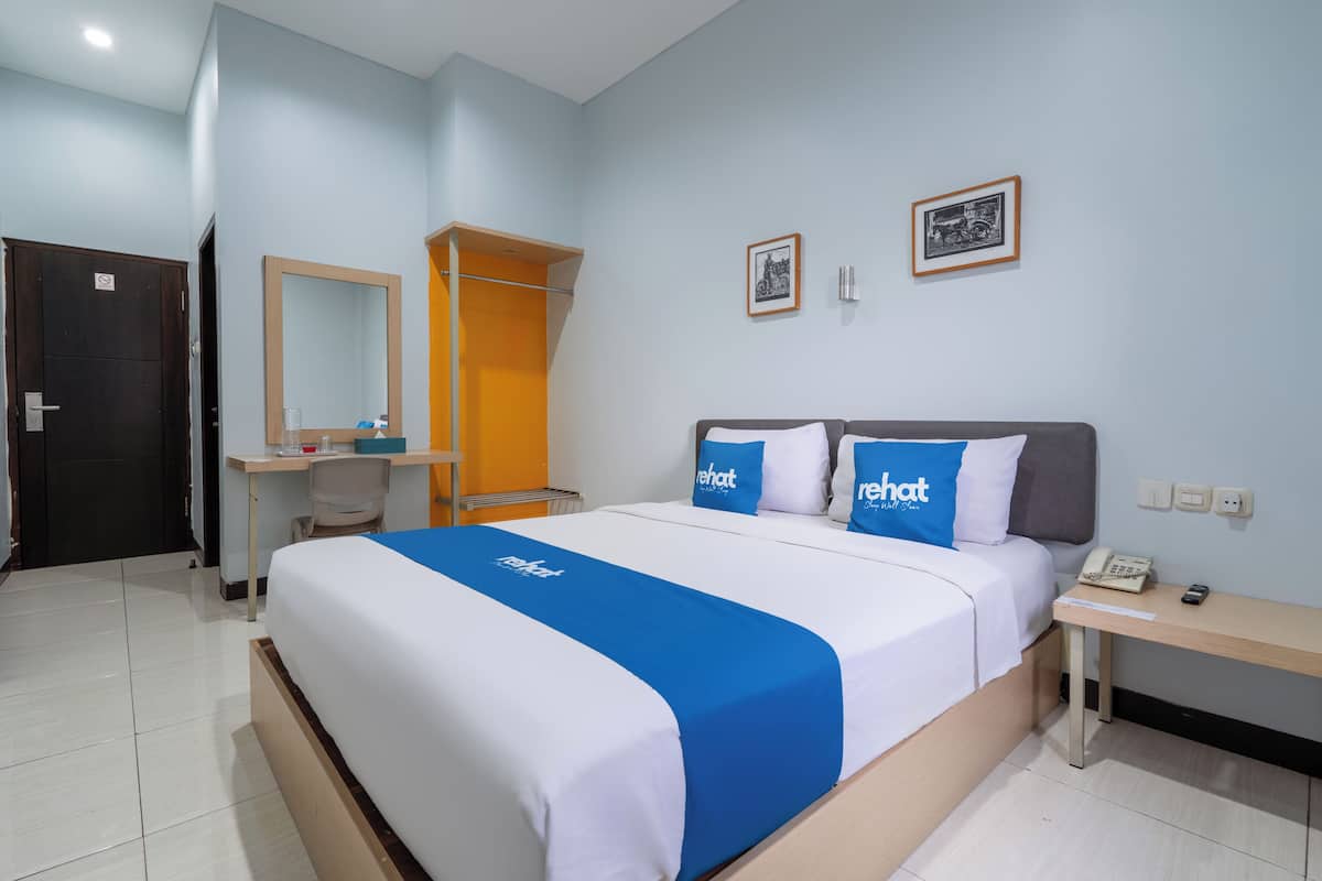 Une chambre d’hôtel avec un lit, un bureau, une armoire et deux tableaux encadrés au mur.