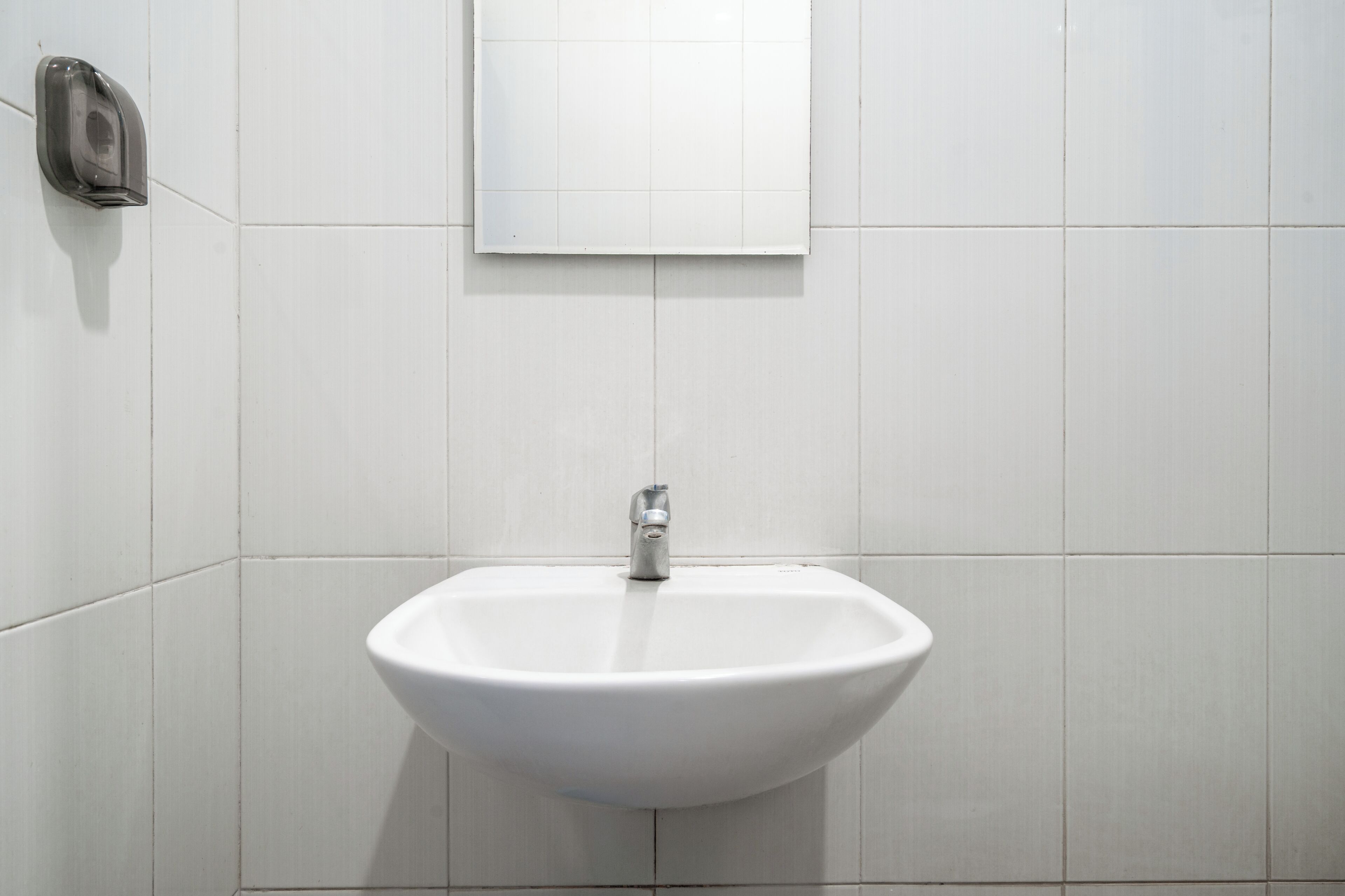 A white bathroom with a sink, a mirror, and a soap dispenser.