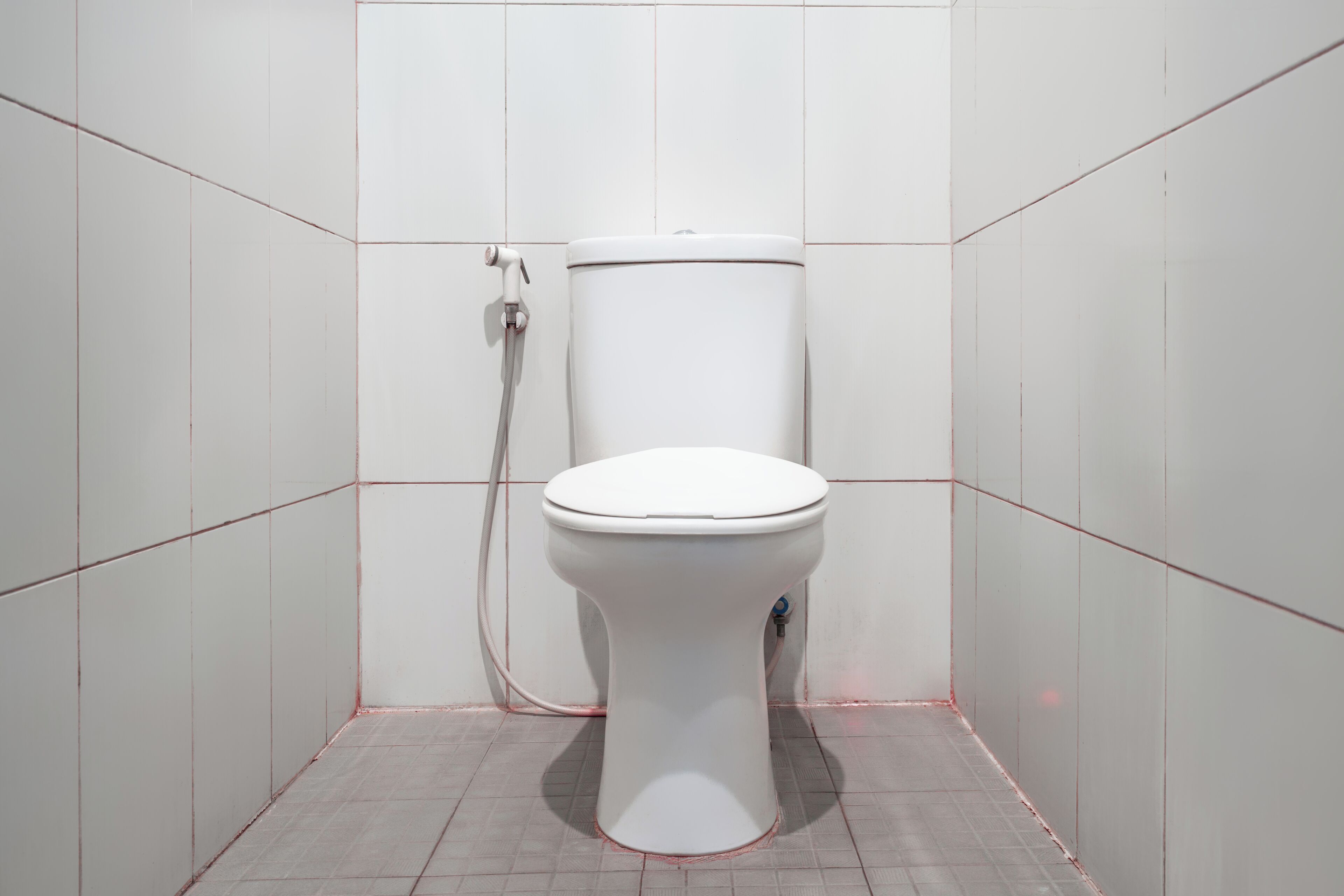Un inodoro en un baño con azulejos blancos en las paredes y el suelo.