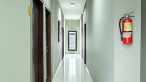 A hotel hallway with a fire extinguisher mounted on the wall, a door with a window, and a sign indicating the direction to the room.