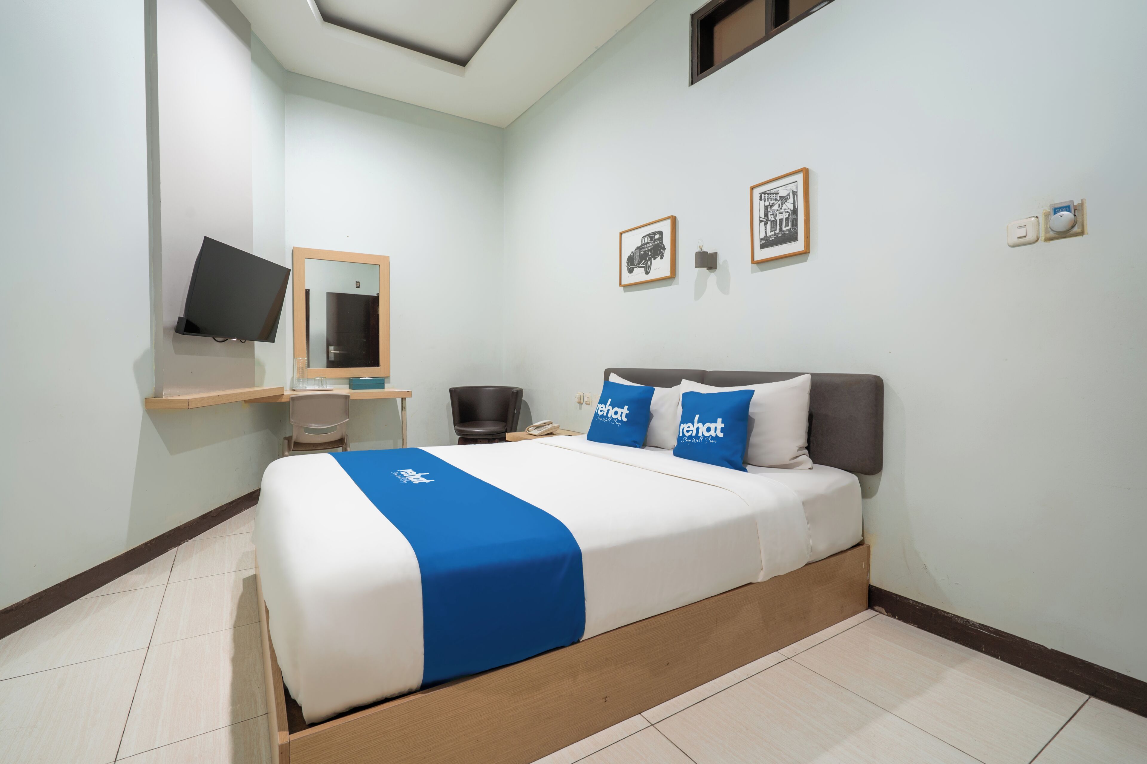 Habitación de hotel con cama, escritorio, silla, televisión y cuadros en la pared.