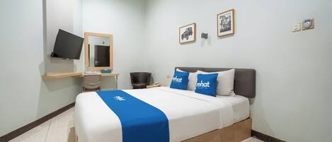 Habitación de hotel con cama, escritorio, silla, televisión y cuadros en la pared.