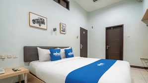 A hotel room with a bed, a bedside table, a desk, and a door.