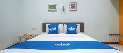 A hotel room with a bed, two pillows with the brand name 'rehat,' a bedside table with a phone, and two framed pictures on the wall.