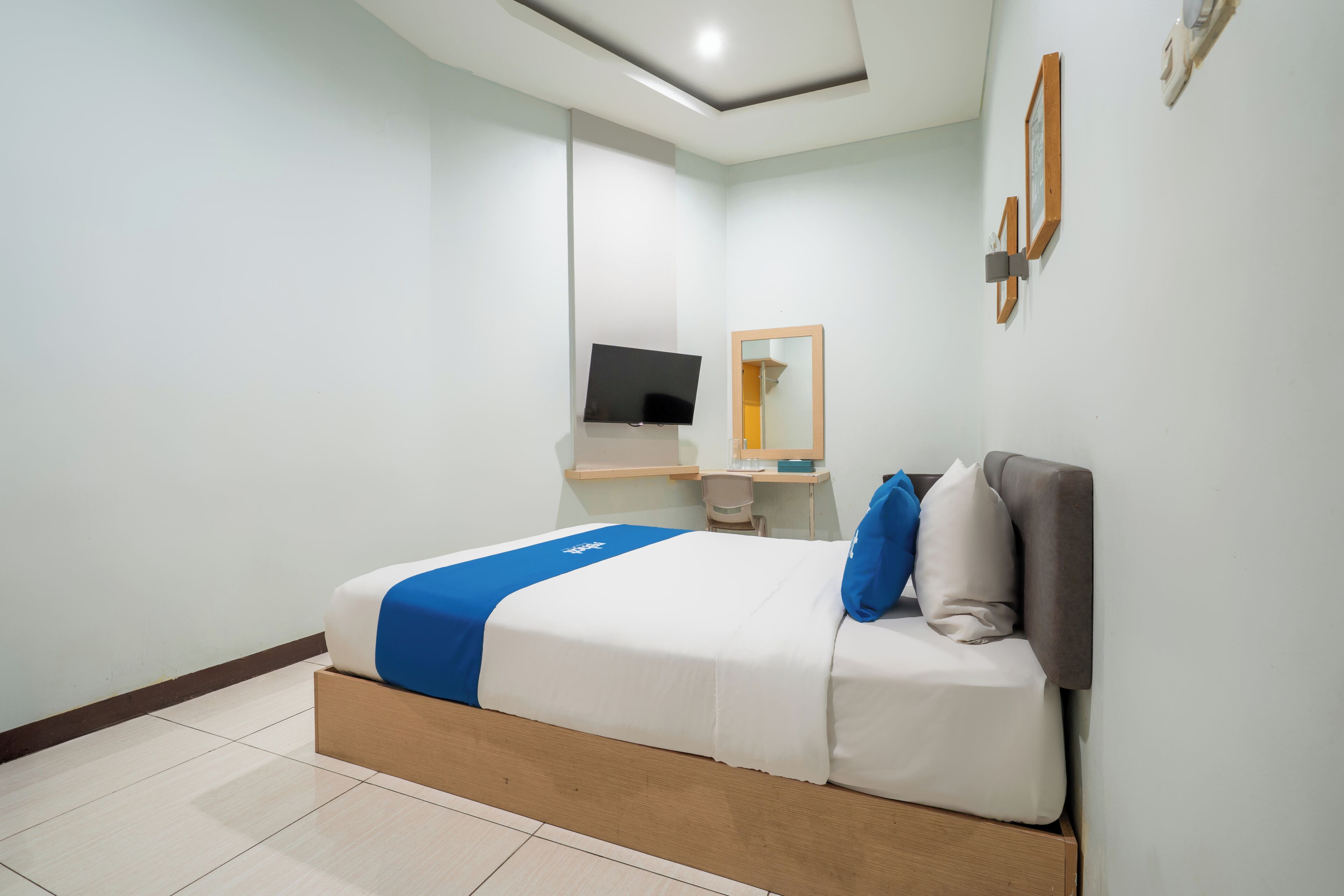 A modern hotel room with a bed, a desk, a chair, a flat-screen TV, and a mirror on the wall.
