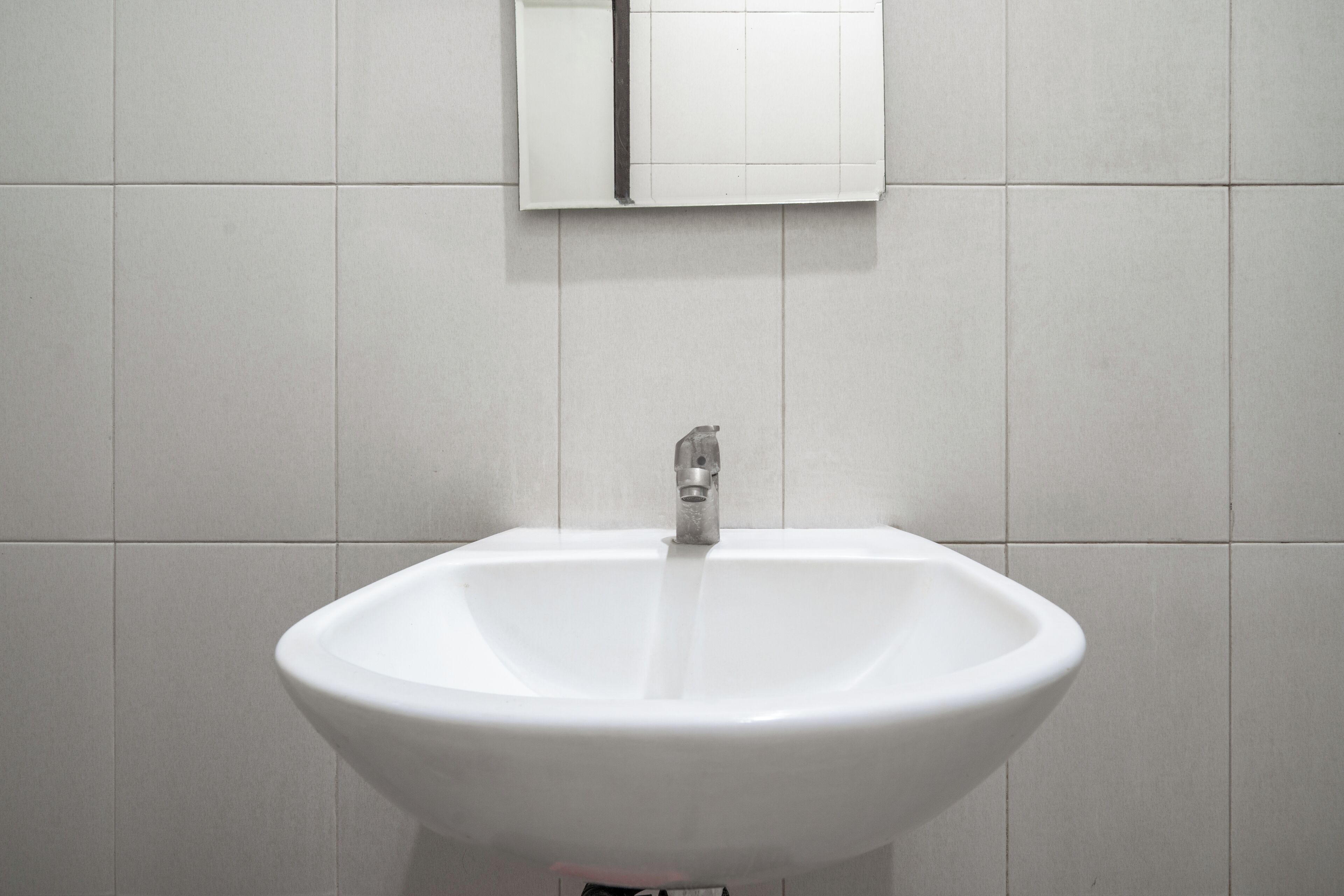 Un lavamanos blanco sobre una pared de azulejos, con un solo grifo.
