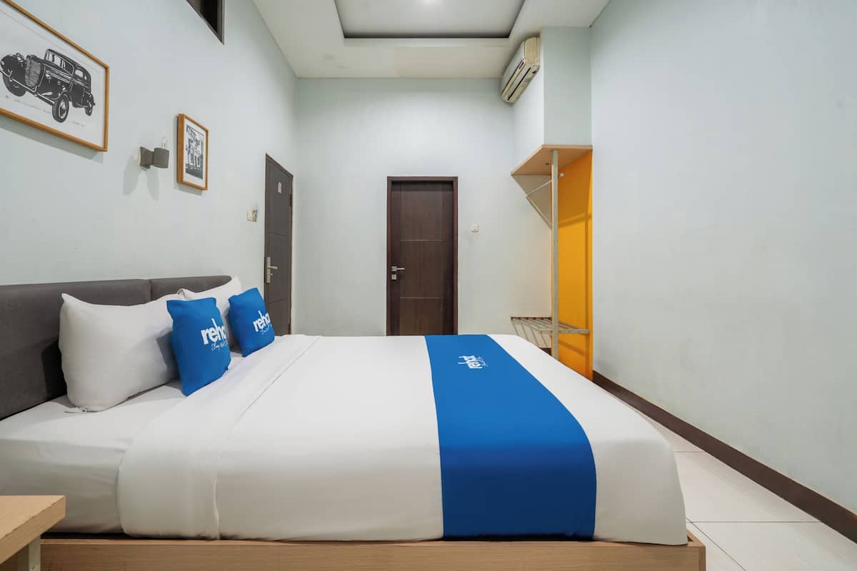 Une chambre d’hôtel avec un lit, une porte, un tableau encadré au mur et un appareil de climatisation.