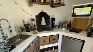 A compact kitchen with a sink, stove, and coffee maker. There are storage baskets and a window above the counter. - Les Savournins Gordes - La Borie des Alpilles (Gordes)