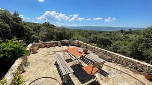 A rustic outdoor patio with a wooden table and benches, surrounded by potted plants and overlooking a mountainous landscape. - Les Savournins Gordes - La Borie des Alpilles (Gordes)