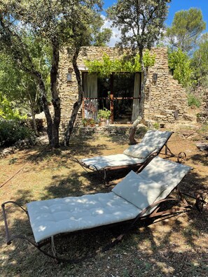 A stone building with a covered patio, two sun loungers, and a stone wall.