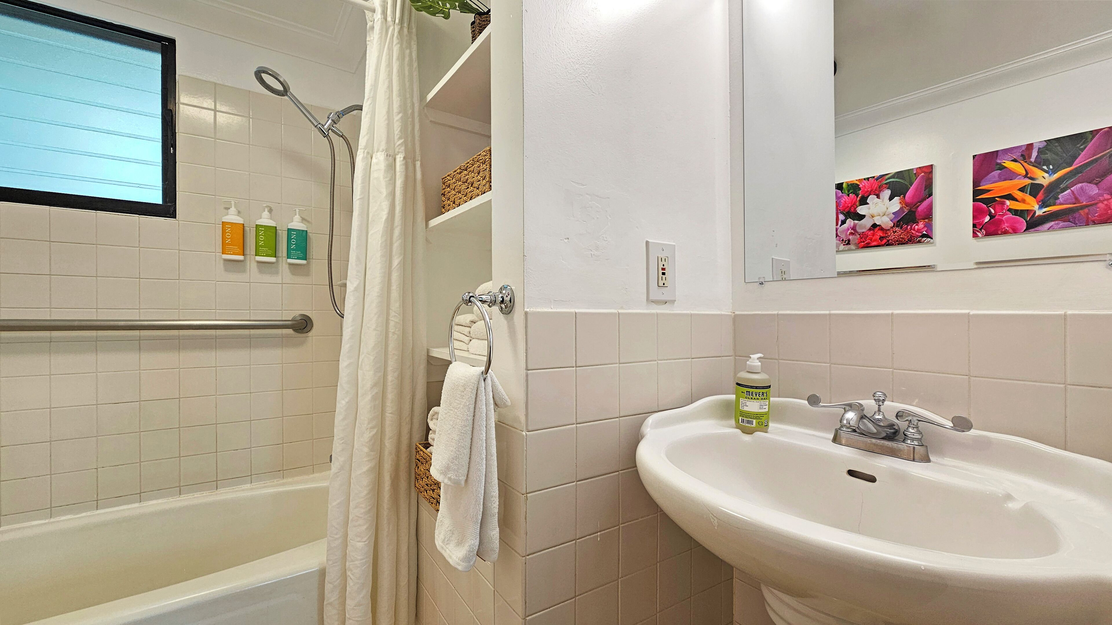 A bathroom with a bathtub, shower, and sink, with toiletries and a mirror.