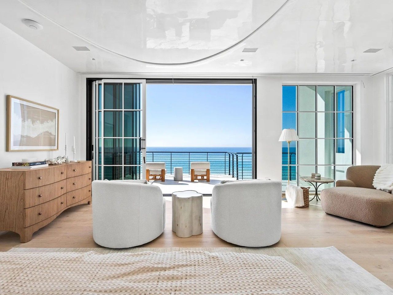 Ein modernes Wohnzimmer mit Blick auf das Meer, einem Holzschrank und einem runden Couchtisch.