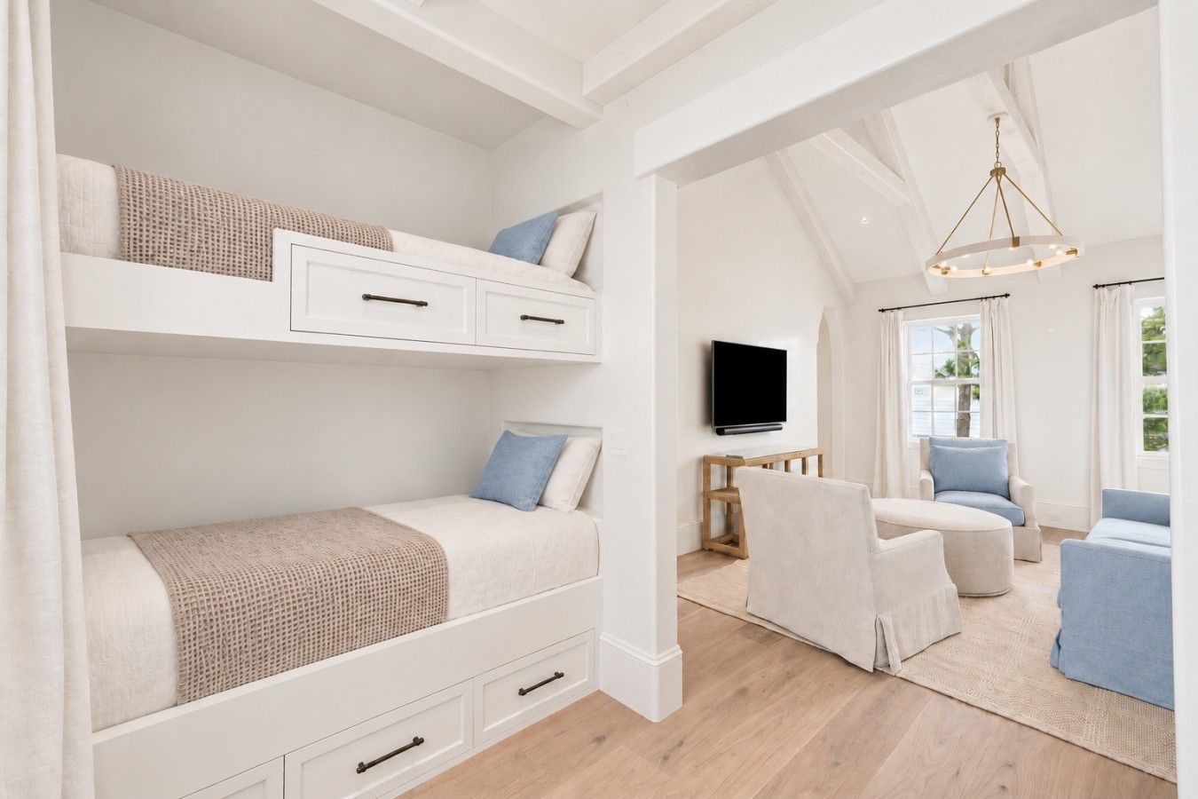 A room with bunk beds, a television, and seating area with a view of the outdoors.