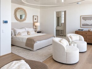 A modern bedroom with a large bed, bedside tables, a mirror, and a seating area with ottomans. - Alys Beach Gulf-Front Estate • Rooftop Pool, Outdoor Kitchen, Private Beach (Alys Beach)