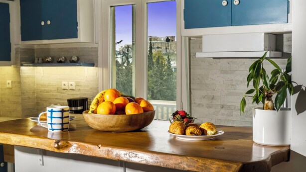 A kitchen with a wooden countertop, a bowl of fruit, a plate of croissants, and a potted plant. - Amazing Acropolis View From A Sunny Renovated Apt in Athens! (Athina)