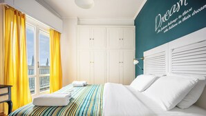 A hotel room with a bed, curtains, a wardrobe, and a wall with a quote. - Amazing Acropolis View From A Sunny Renovated Apt in Athens! (Athina)