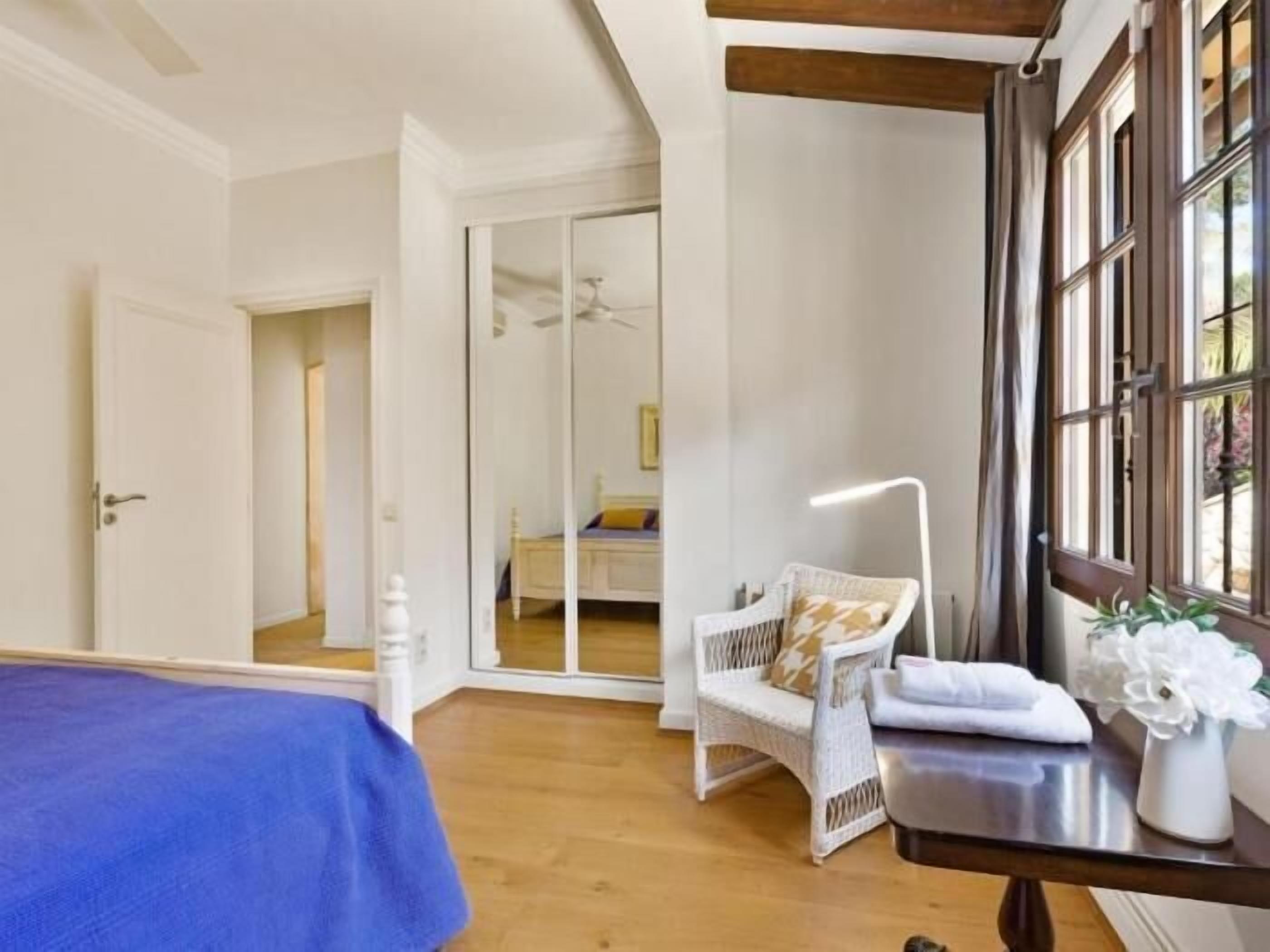 Een slaapkamer met een bed, een stoel, een tafel met een lamp en een raam.