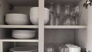 A kitchen with white cabinets, shelves with stacked plates, bowls, and clear glassware. - Le Yellow: Design Studio, Fibre, Metz Center (Metz)