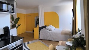 A compact hotel room with a kitchenette, a bed, a dining area, and a mirror. - Le Yellow: Design Studio, Fibre, Metz Center (Metz)