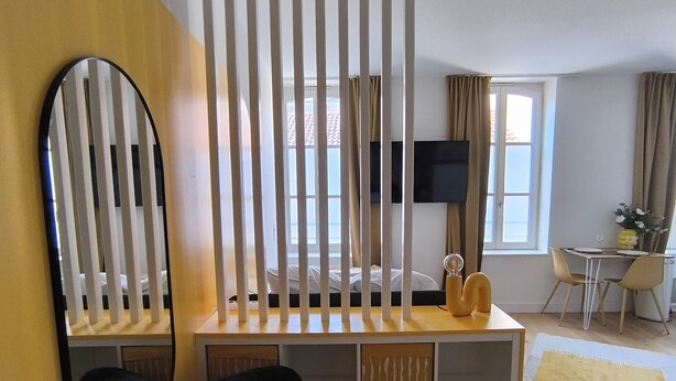 A modern room with a black chair, a wooden desk, a TV, and a bed with curtains. - Le Yellow: Design Studio, Fibre, Metz Center (Metz)
