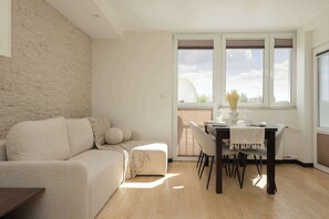 A modern living room with a sofa, a dining table with chairs, and large windows. - Family Apartment | Workplace, Close to Metro (Warszawa)