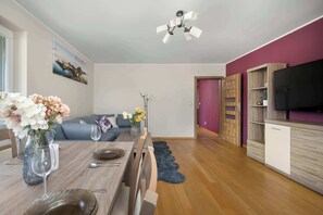 Een eetruimte met een tafel gedekt voor twee personen, een vaas met bloemen, een plafondventilator en een televisie op de achtergrond.