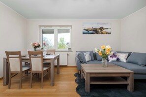 Een woonkamer met een bank, een salontafel, een eettafel met stoelen en een raam met uitzicht.
