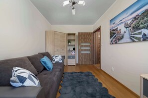 Een moderne woonkamer met een bank, een vloerkleed, een plafondventilator, houten kasten en een schilderij van een kustlandschap.