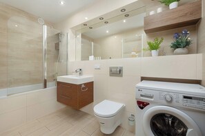 A modern bathroom with a glass shower enclosure, a toilet, a washing machine, and a vanity with a mirror. - Family Apartment in Wroclaw | Balcony | Parking | 2 Bedrooms (Wrocław)