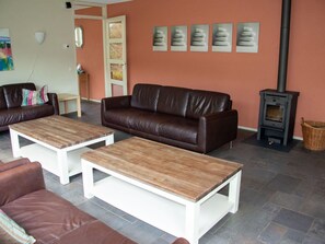 Ein Wohnzimmer mit einem braunen Ledersofa, zwei Holztischen, einem Kamin und einer Wand mit gerahmten Bildern.