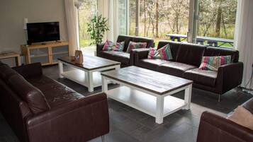 A modern living room with leather sofas, white coffee tables, and a TV on a wooden stand.