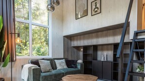 Ein modernes Wohnzimmer mit einem grünen Sofa, einem Holztisch und einem großen Fenster mit Blick auf Bäume.