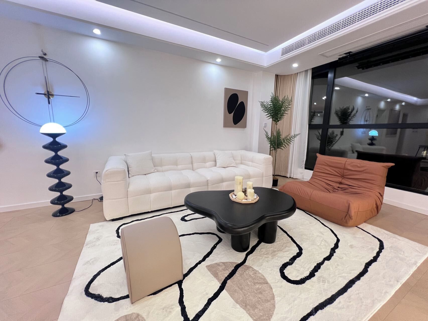 A modern living room with a sofa, a black coffee table, a beige ottoman, and a floor lamp.