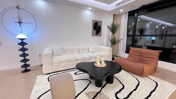 A modern living room with a sofa, a black coffee table, a beige ottoman, and a floor lamp.