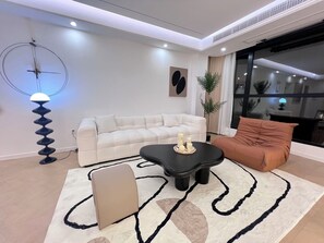 Ein modernes Wohnzimmer mit einer Couch, einem schwarzen Couchtisch, einem beigen Hocker und einer Stehlampe.