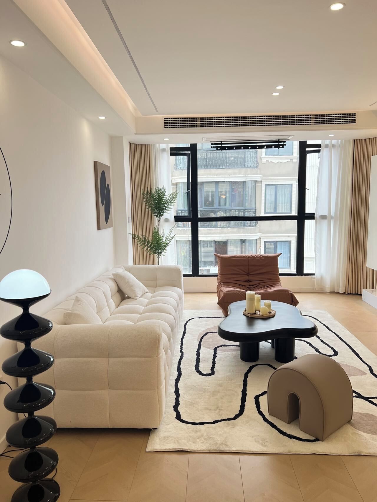 Ein modernes Wohnzimmer mit Sofa, Couchtisch, Lampe und Blick auf ein Gebäude durch große Fenster.