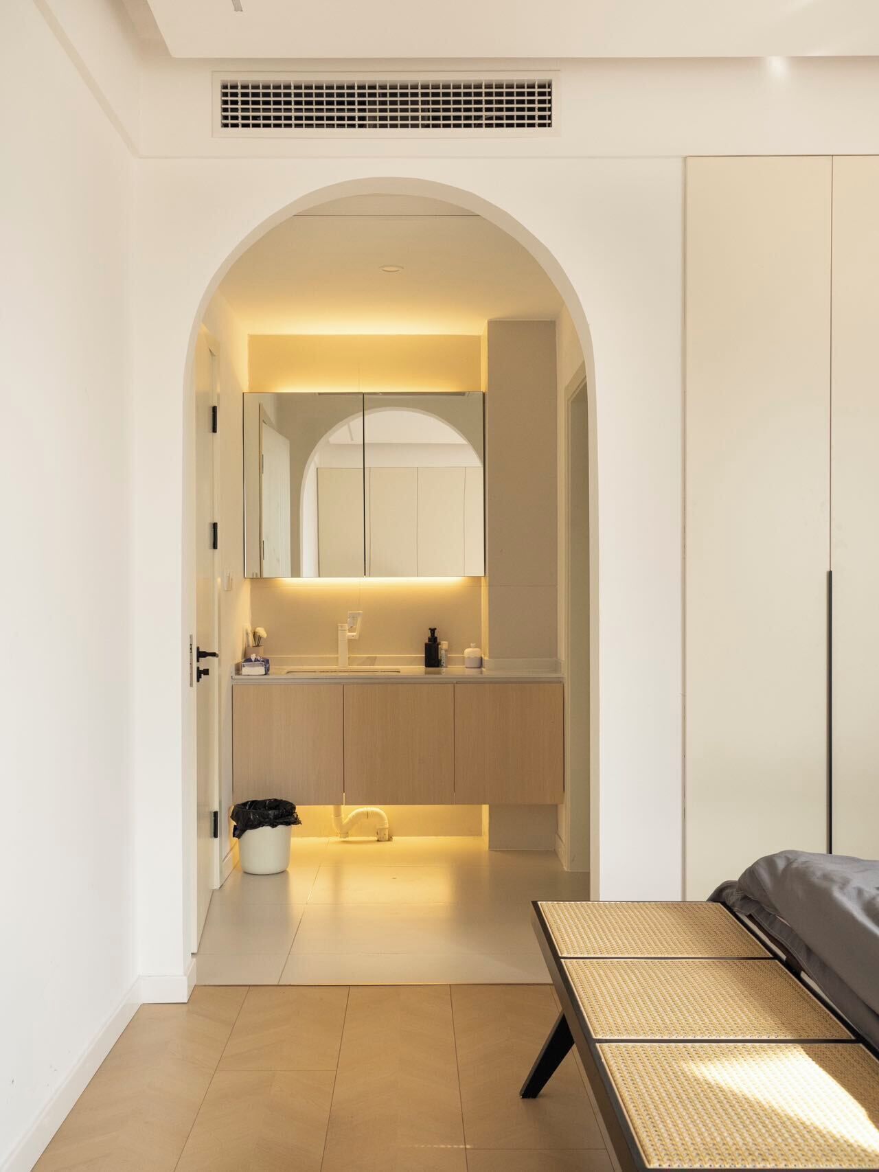 A modern bedroom with a bed, a small bedside table, a large mirror, and a wardrobe.