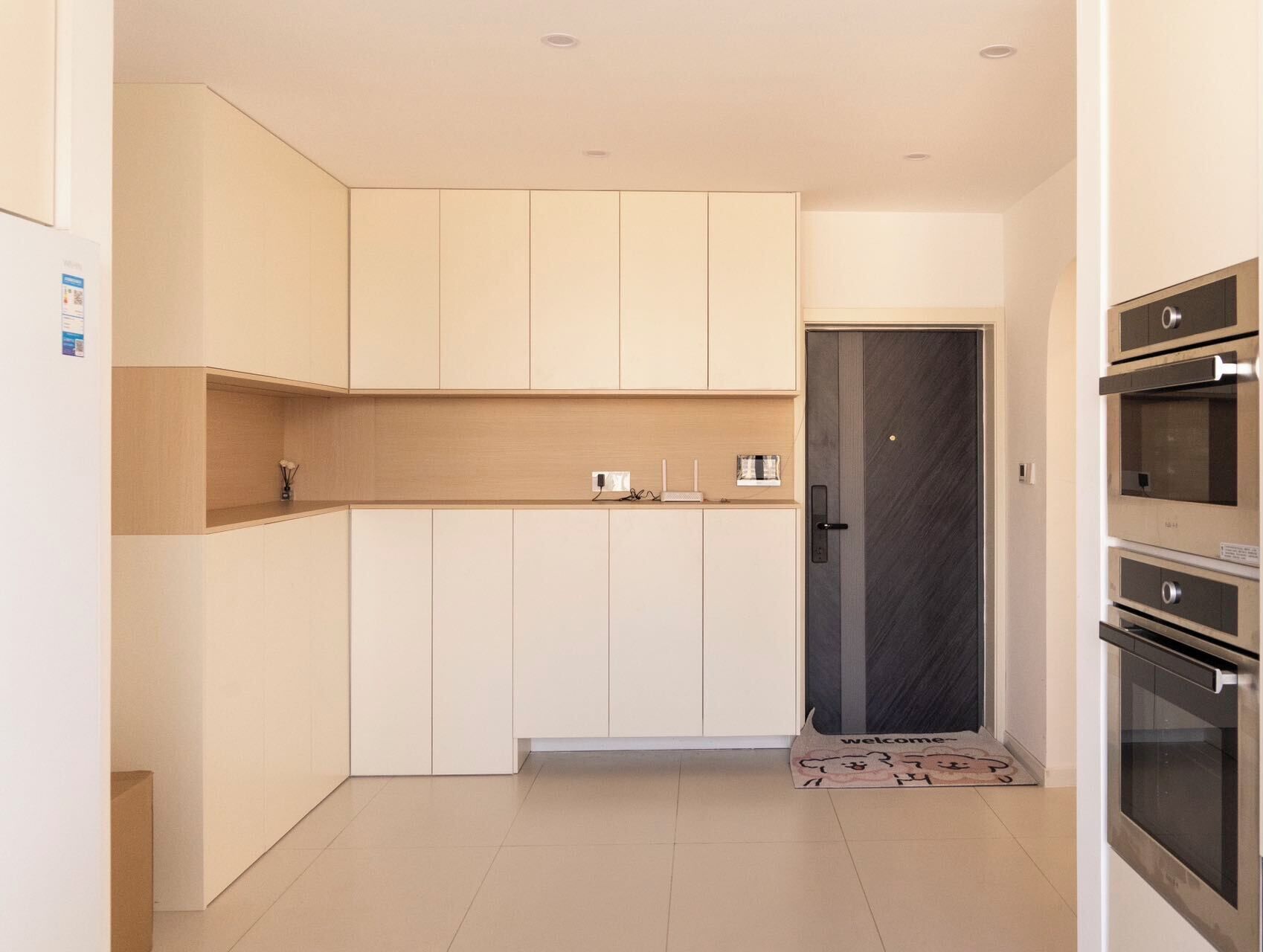 A modern kitchen with white cabinets, a dark door, and built-in appliances.