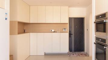 A modern kitchen with white cabinets, a dark door, and built-in appliances.