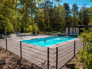 Ein rechteckiger Pool, umgeben von einem Metallzaun, mit Liegestühlen und einem überdachten Sitzbereich.