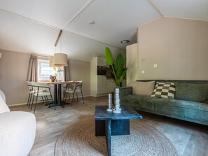 A modern living room with a sofa, a dining table with chairs, a coffee table, and a large plant. - Vakantiepark De Wiltzangh - Veenborg Lodge by Interhome (Ruinen)