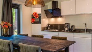 Una cocina moderna con comedor, que incluye una mesa de madera oscura, sillas tapizadas en verde, una lámpara colgante y una estatua de Buda en la pared.