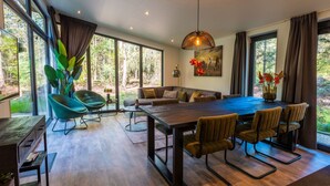 Un comedor moderno con una mesa grande, sillas y vistas al bosque a través de amplios ventanales.