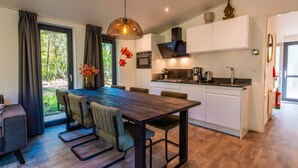 Una cocina moderna con armarios blancos, una zona de comedor con una mesa y sillas de madera oscura, y vistas a la vegetación exterior.