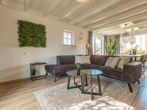 A modern living room with a sectional sofa, a coffee table, a wall-mounted plant, and a dining area with a table and chairs. - Vakantiepark Wiedense meren - Weerribben by Interhome (Wanneperveen)