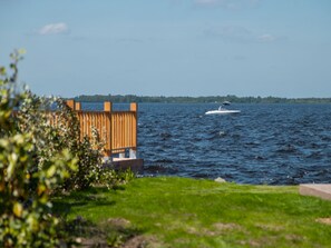 A waterfront view with a wooden structure, a boat on the water, and a distant shoreline. - Vakantiepark Wiedense meren - Chalet Comfort + by Interhome (Wanneperveen)