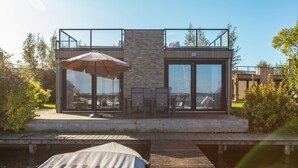Ett modernt hus med ett glashus, en träveranda och utsikt över vattnet.